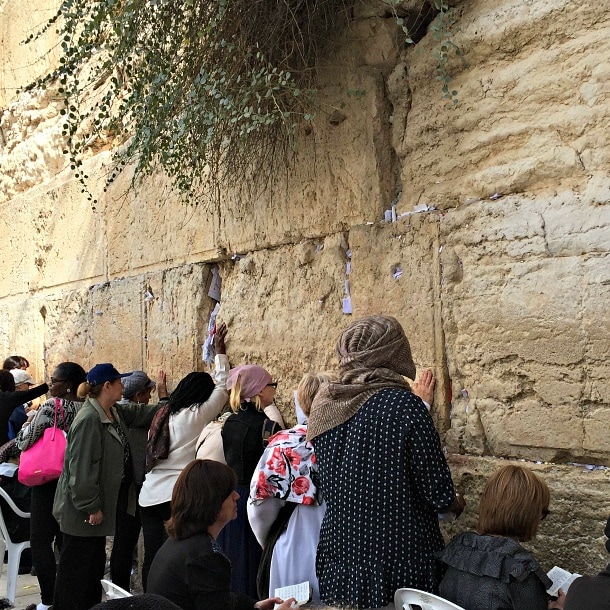 Women praying and placing notes in the Western Wall