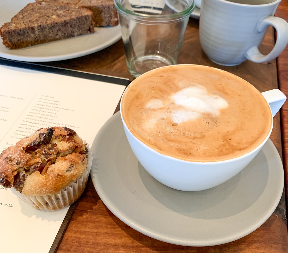 A gluten-free mini date muffin and an almond milk latte with banana bread in the background at Campo, Los Poblanos Farm near Albuquerque