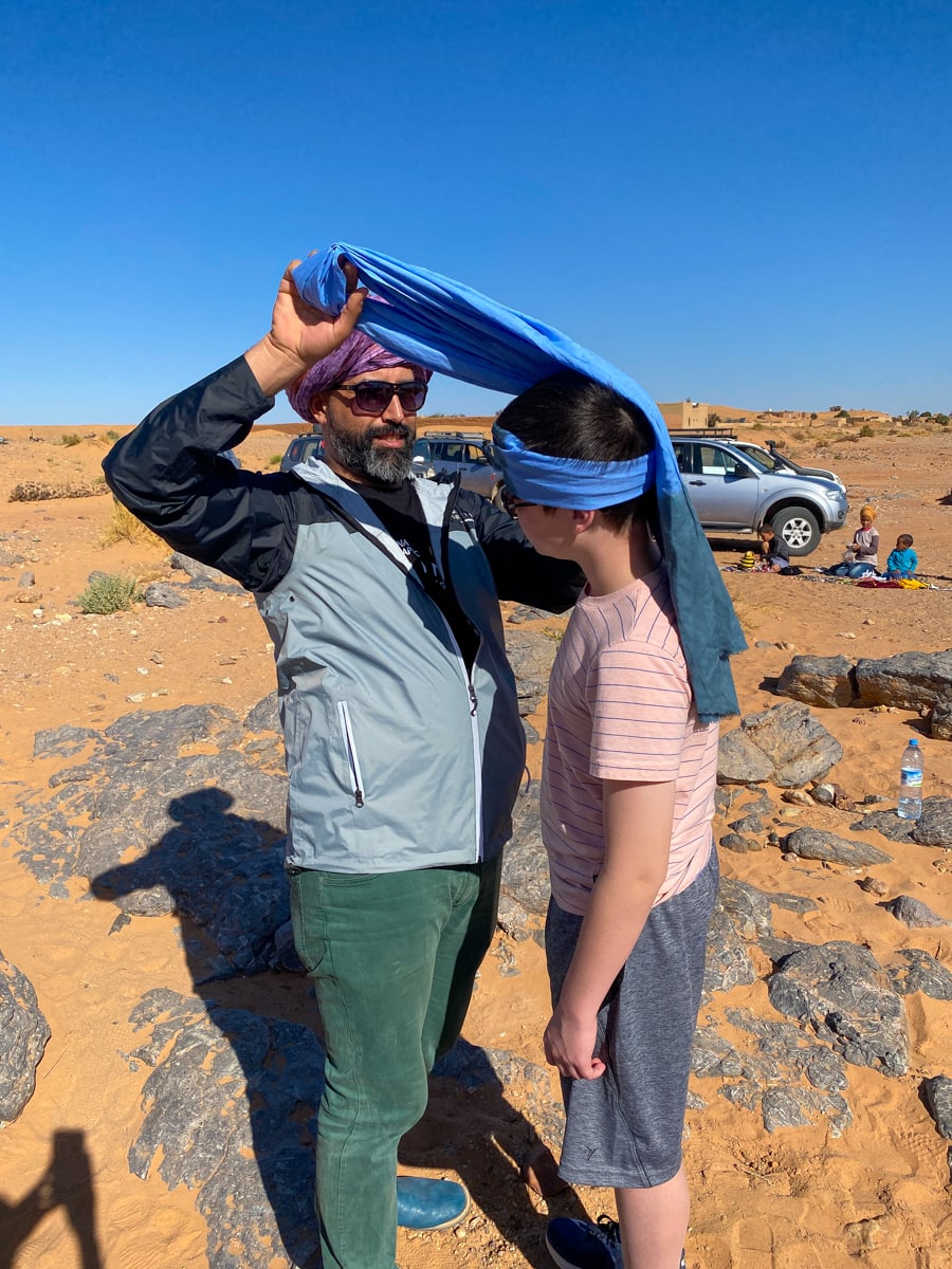National Geographic & G Adventures guide tying a headscarf for a child in the Sahara Desert